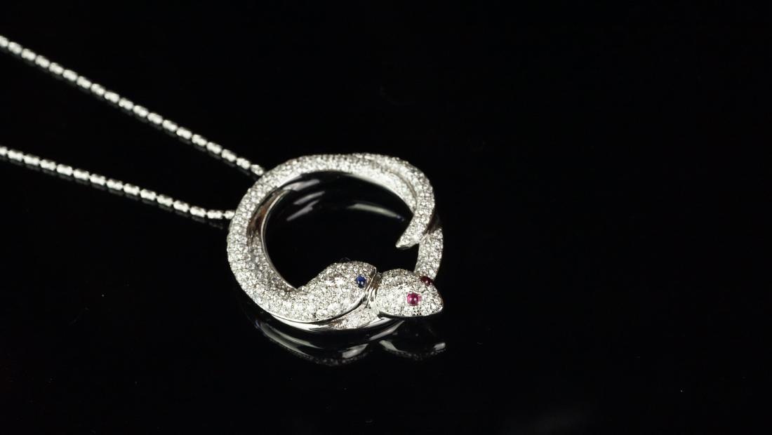 Diamond set double entwined snake pendant mounted in: Diamond set double entwined snake pendant mounted in white metal stamped 'K18WG', one snake with cabochon ruby set eyes and the other with cabochon sapphire set eyes, set with diamonds, with a 44cm fa