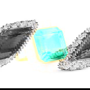 A FINE COLOMBIAN EMERALD AND DIAMOND RING in 18ct yellow gold, set with an octagonal step cut: A FINE COLOMBIAN EMERALD AND DIAMOND RING in 18ct yellow gold, set with an octagonal step cut emerald of approximately 15.58 carats in a cluster of round brilliant cut diamonds, the shoulders set with