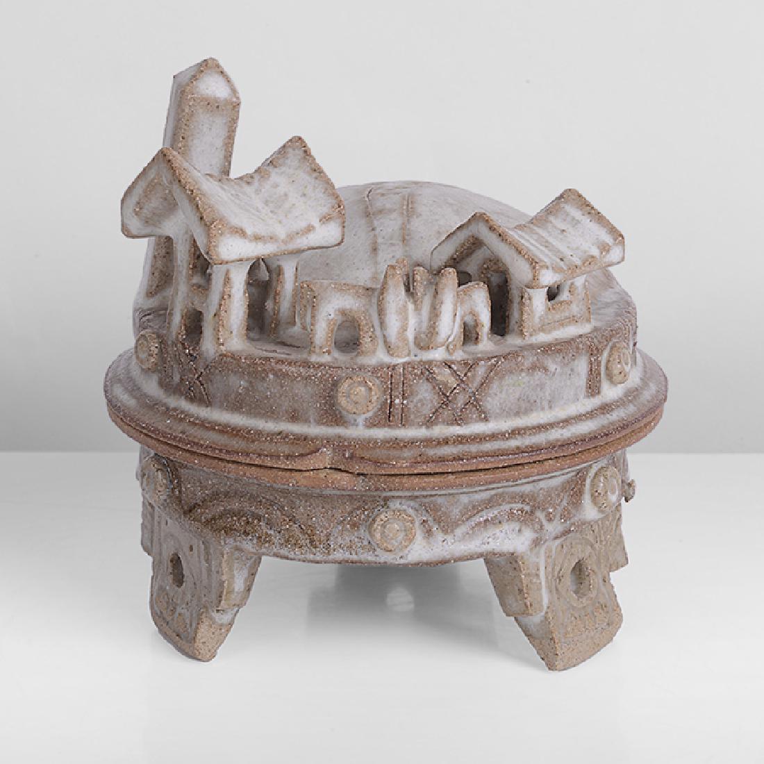 Ian Godfrey (British, 1942-1992): Village Casket, circa 1978 Stoneware, splashed white over transparent grey green glazes, the domed lid encrusted with beasts amongst huts and an obelisk, a hill with huts and birds within, raised on t