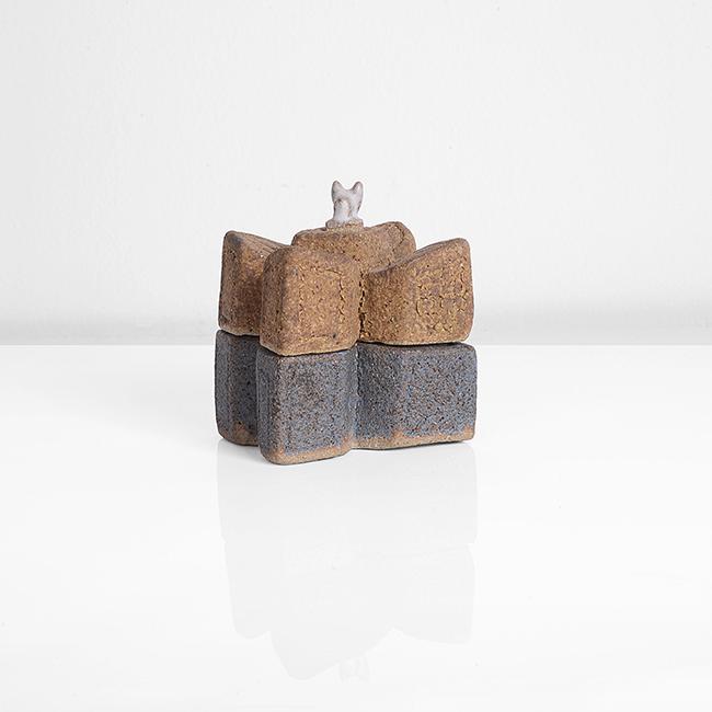 Ian Godfrey (British, 1942-1992): Lidded Box, circa 1974 Stoneware, cross formed box with carved surface, the base with matt blue glaze, the lid with brown glaze, ta small white beast set into the lid DIMENSIONS: H 6.3cm, W 5.0cm, D 4