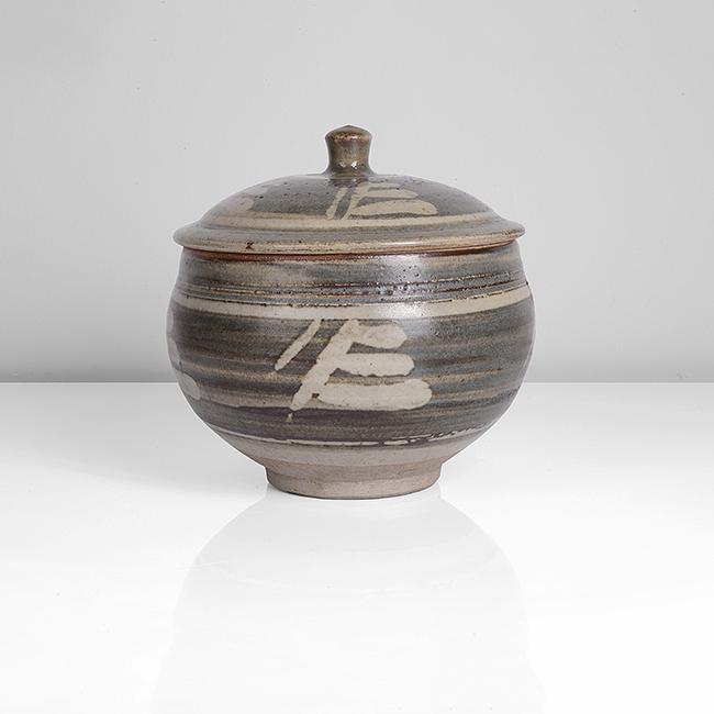 Bernard Leach (British, 1887-1979): Lidded Jar, circa 1936 Stoneware, brushed blue over cream and iron glazes, wax resist calligraphic decoration around the body and to the domed lid, incised BL and impressed Leach Pottery seal Dimensio