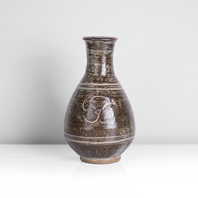 Bernard Leach (British, 1887-1979): Vase Stoneware, layered grey and iron glazes with incised floral design repeated around the body, impressed BL and Leach Pottery seals Dimensions: H 22.2.cm, D 13.7cm PROVENANCE: Dr John P Driscoll Co