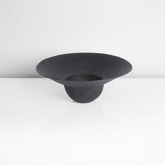 John Ward (British, b. 1938): Flanged Bowl', 2004 Stoneware, black glaze over a softly textured surface, the rounded bowl form with broad flaring rim, impressed JW seal Dimensions: H 9.8cm, D 25.4cm PROVENANCE: Private Collection,