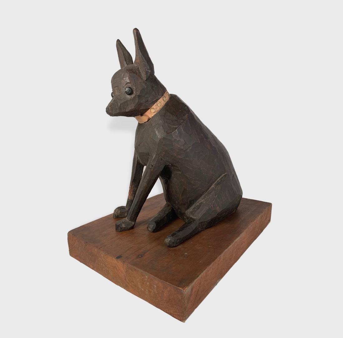 Seated Dog Sculpture By Anne Arnold: A carved and painted wood sculpture of a seated dog by artist Anne Arnold (1925-2004), Signed and dated 1964 on base. Minor damage to leg and ears. Dimensions: 14.5" w x 10" d x 15" h