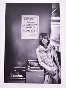 The Rolling Stones: a black and white photograph of: The Rolling Stones: a black and white photograph of Keith Richards taken by Ethan Russell, with Richards standing in sunglasses beside a poster reading 'Patience Please...A Drug Free America Comes Fir