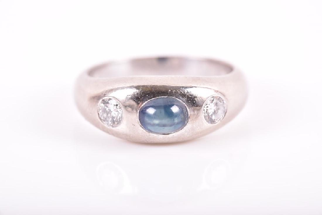 A diamond and sapphire ring centred with a rounded: A diamond and sapphire ring centred with a rounded cabochon sapphire flanked with two round-cut diamonds inset to shank, stamped 750, size G 1/2, 5.4 grams.