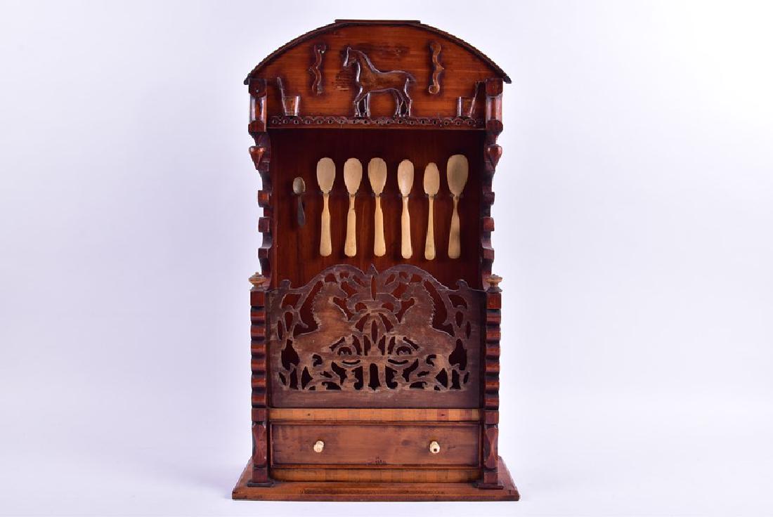 A early 19th century American spoon rack with fretwork: A early 19th century American spoon rack with fretwork panel of horse motifs (split), the domed pediment with carved horse and various tools (small loss), six antique bone spoons and a small horn exam