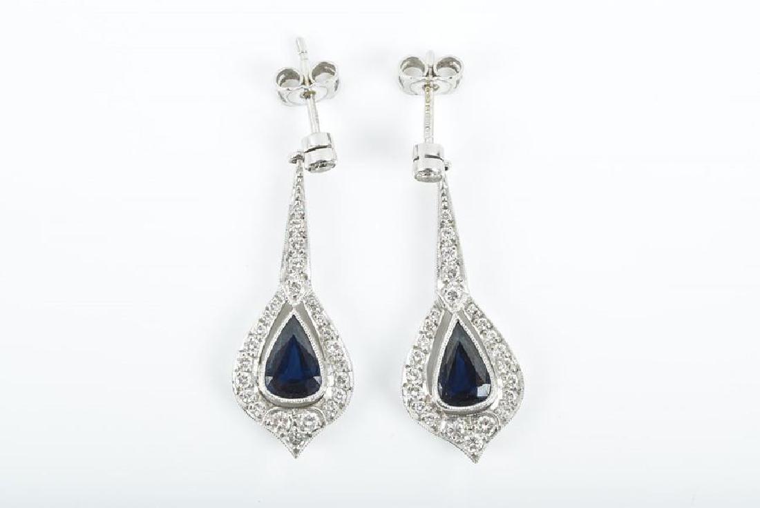 A pair of 18ct white gold, diamond, and sapphire drop: A pair of 18ct white gold, diamond, and sapphire drop earrings the tapered mount suspended with a pear-shaped drop set with a sapphire surrounded with diamonds, 3.7 cm long.