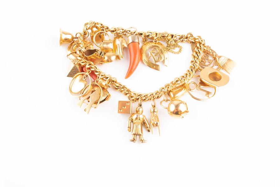 A yellow metal curb-link charm bracelet bearing: A yellow metal curb-link charm bracelet bearing Egyptian marks, suspended with various yellow metal charms, including a turtle, lovebirds, a coral figa, a pyramid, a stetson hat, a watering can, etc.