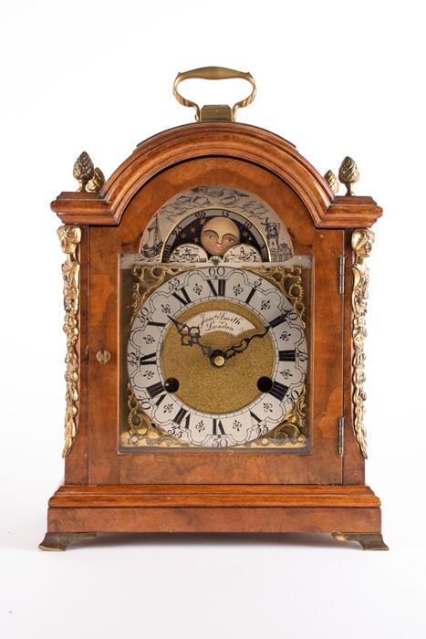 A German burr walnut moonphase mantle clock by James: A German burr walnut moonphase mantle clock by James Smith, London, with Roman numeral dial, the case mounted with brass busts to the front corners, the top with brass handle and pine cone finials,