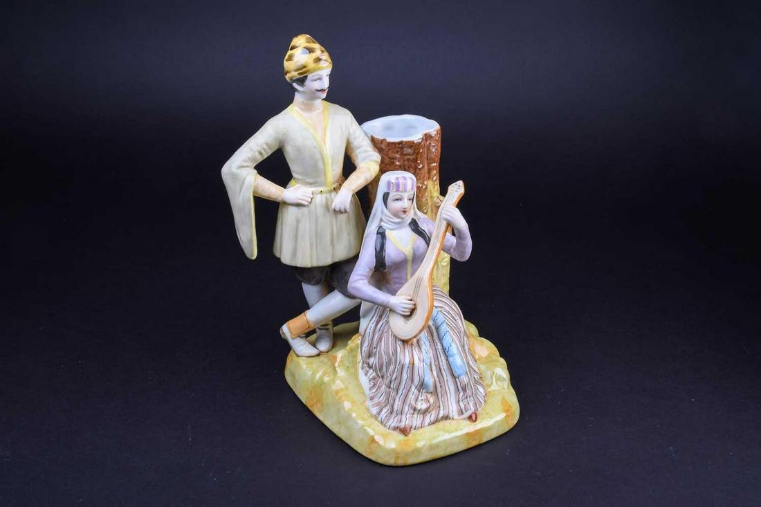 A Russian Gardner porcelain figure group, a seated: A Russian Gardner porcelain figure group, a seated female musician before a tree stump, with a man in traditional dress, red printed mark to base, 26 cm high.