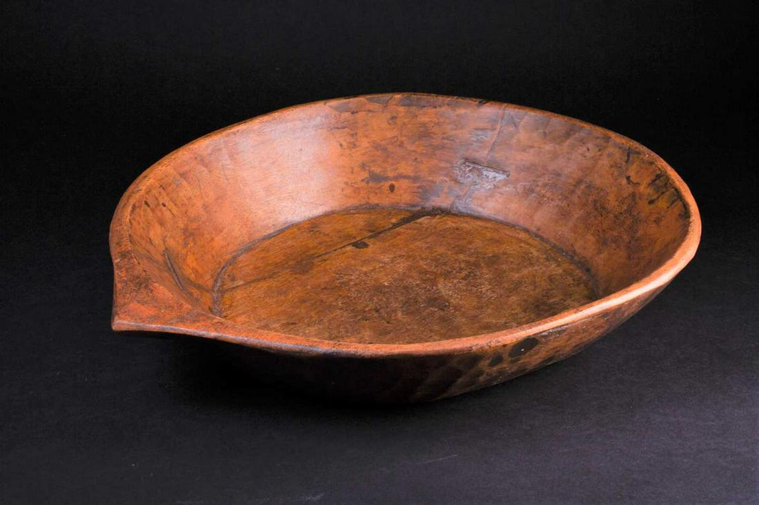 An Indian carved wood bowl, the rim terminating in a: An Indian carved wood bowl, the rim terminating in a point, the exterior with adzed sloping sides, a metal rivet repair, 45.5cm x 38cm Footnote: The late Reverend Alan Dupuy
