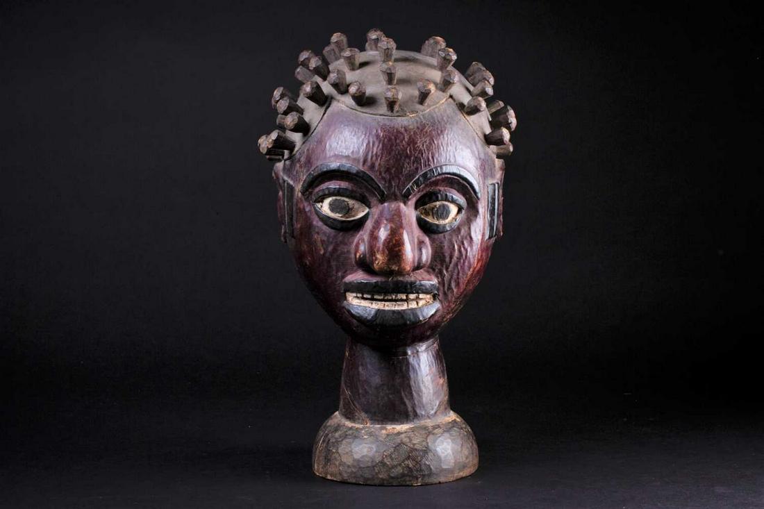 An Ejagham (Ekoi) leather bound carved wood headpiece,: An Ejagham (Ekoi) leather bound carved wood headpiece, the head with numerous inset pegs, the maroon coloured leather with painted eyebrows, eyes, lips and teeth, with scarification marks to the sides