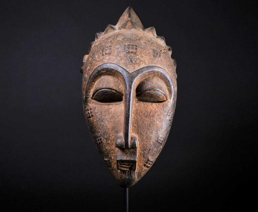 A Punu mask, Gabon, with short linear coiffure within: A Punu mask, Gabon, with short linear coiffure within short knots, the forehead and face with groups of nine small square scarification marks, with rectangular mouth above a short beard, painted in a 