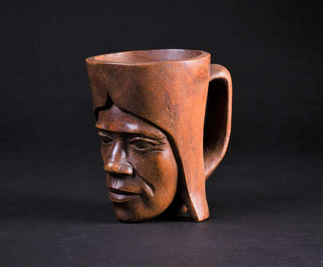 An African carved wood palm wine cup, third quarter: An African carved wood palm wine cup, third quarter 20th century, carved from a single piece of wood with a male bust in headdress, 13cm high, interior diameter 8.4cm Footnote: The late Reverend Alan 