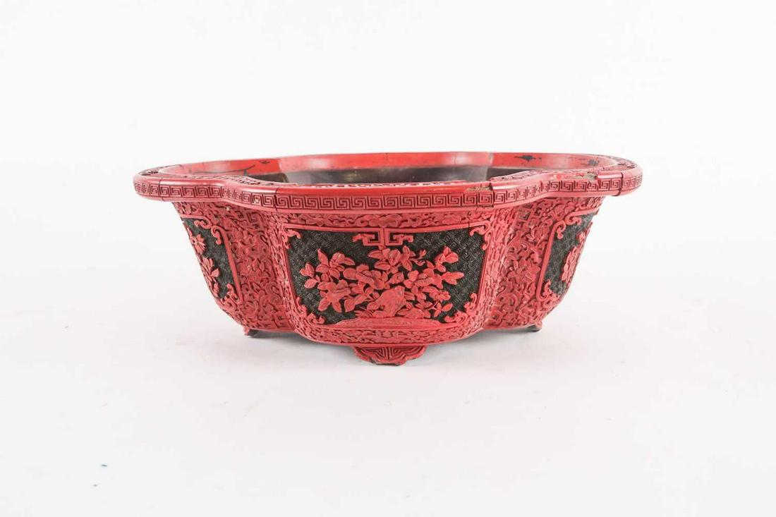 A Chinese cinnabar lacquer bowl, of shaped oval form,: A Chinese cinnabar lacquer bowl, of shaped oval form, with floral decorated reserves, 10 cm high x 28 cm wide.