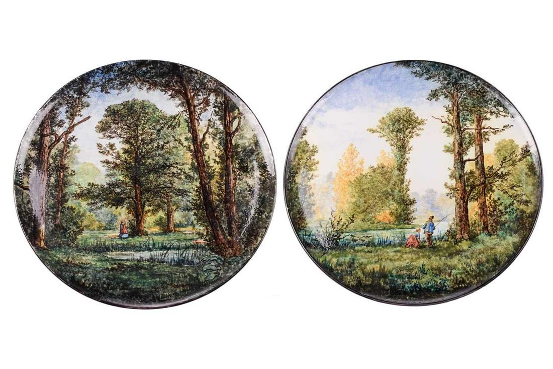 A pair of Gien pottery chargers, early 20th century, signed A Marois, painted with a couple walking: A pair of Gien pottery chargers, early 20th century, signed A Marois, painted with a couple walking by a pond through the woods and a young couple fishing on a riverbank, each also signed verso, facto