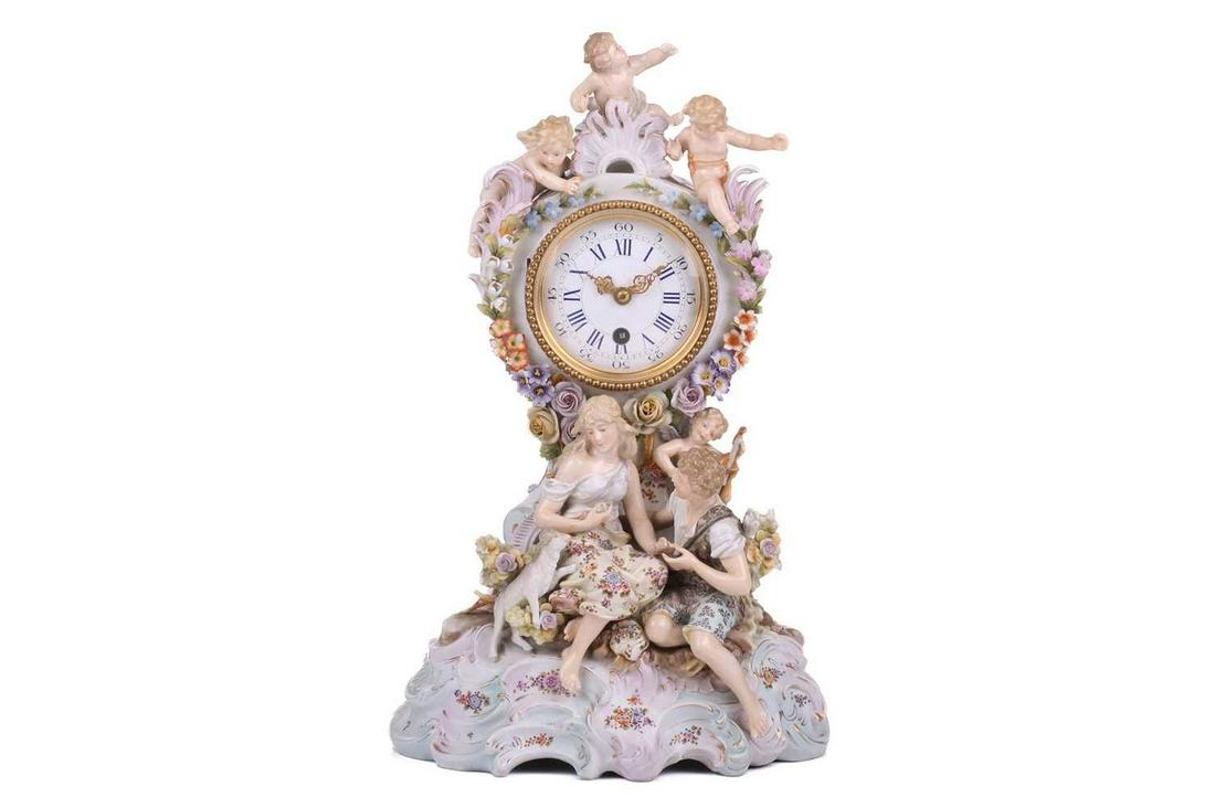A Volkstedt porcelain figural mounted mantel timepiece, late 19th century, mounted with a seated: A Volkstedt porcelain figural mounted mantel timepiece, late 19th century, mounted with a seated courting couple observed from above by amorini, decorated with applied and painted blooms on a domed sc