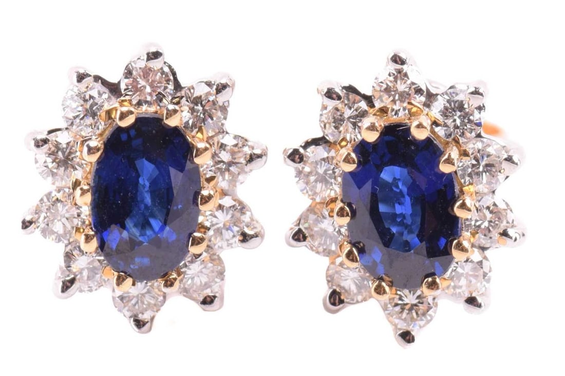 A pair of diamond and sapphire earrings; the oval cut sapphire claw mounted within a border of ten: A pair of diamond and sapphire earrings; the oval cut sapphire claw mounted within a border of ten round brilliant cut diamonds, to 18-carat white gold post fittings.11 mm, 3.8 grams.