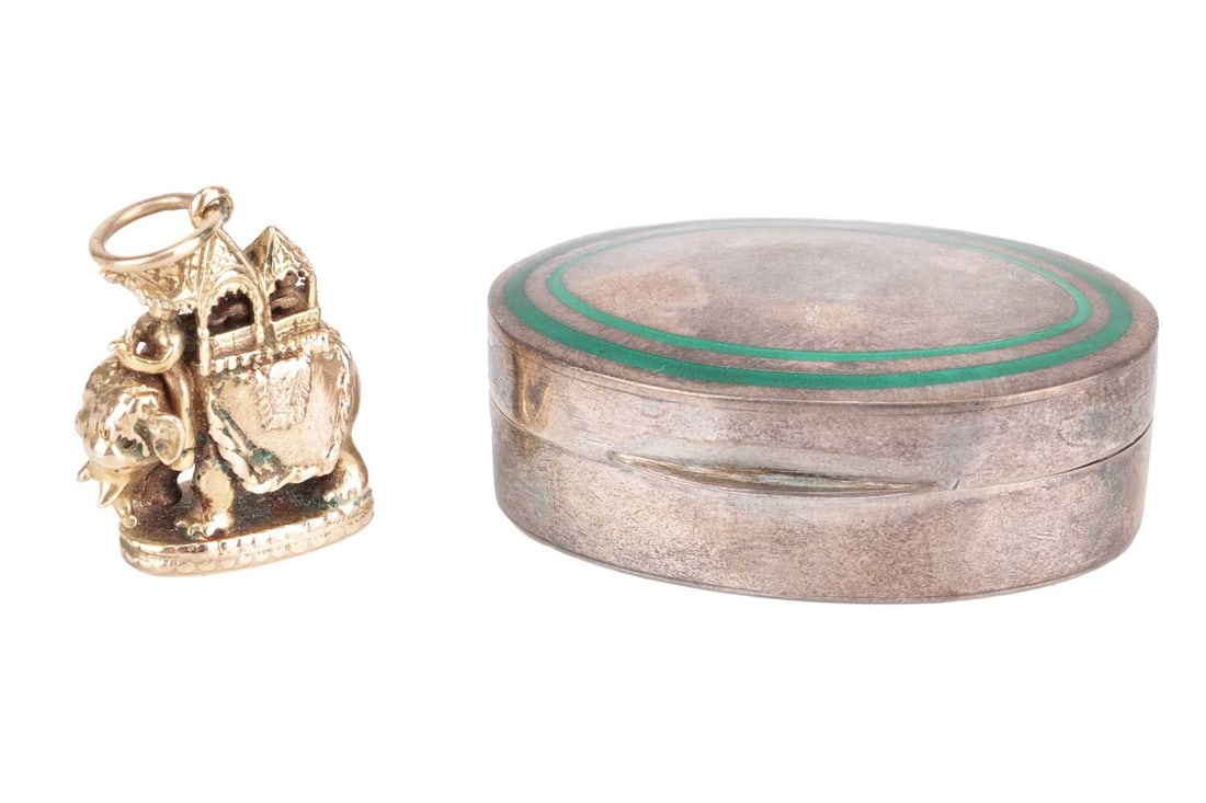 A 9ct yellow gold charm depicting an elephant and howdah, 8.2 grams; together with a Cartier white m: A 9ct yellow gold charm depicting an elephant and howdah, 8.2 grams; together with a Cartier white metal and enamel oval pill box, stamped '925' and 'sterling' with maker's mark 'Cartier'; 17.7 grams