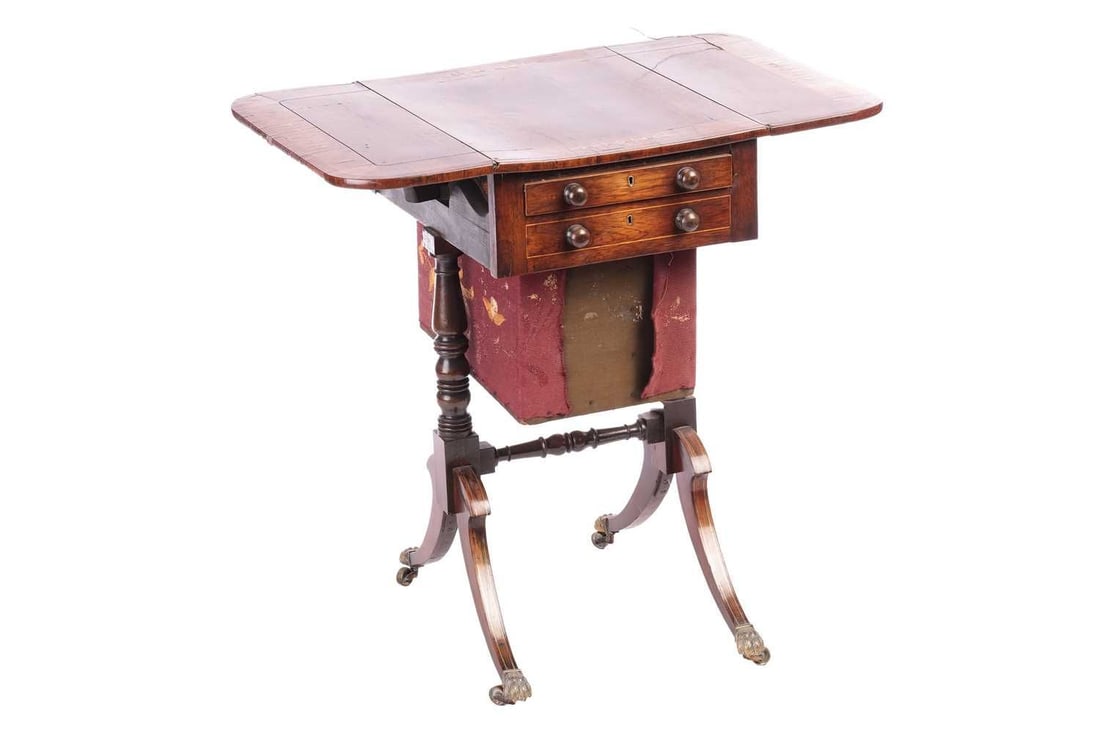 In the manner of John McLean; a Regency brass inlaid figured rosewood two-flap work table, fitted: In the manner of John McLean; a Regency brass inlaid figured rosewood two-flap work table, fitted one faux and one actual frieze drawer with work bag below supported by end stiles with haunched sabre