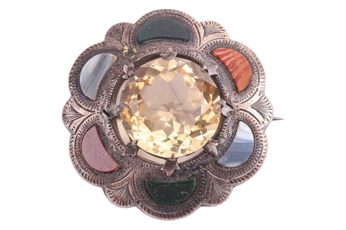 A Scottish hardstone brooch set with a large faceted citrine, to a scalloped surround adorned with p: A Scottish hardstone brooch set with a large faceted citrine, to a scalloped surround adorned with polished jasper, banded agate and bloodstone, Birmingham 1912, 4.2 cm wide, 16.0 grams.