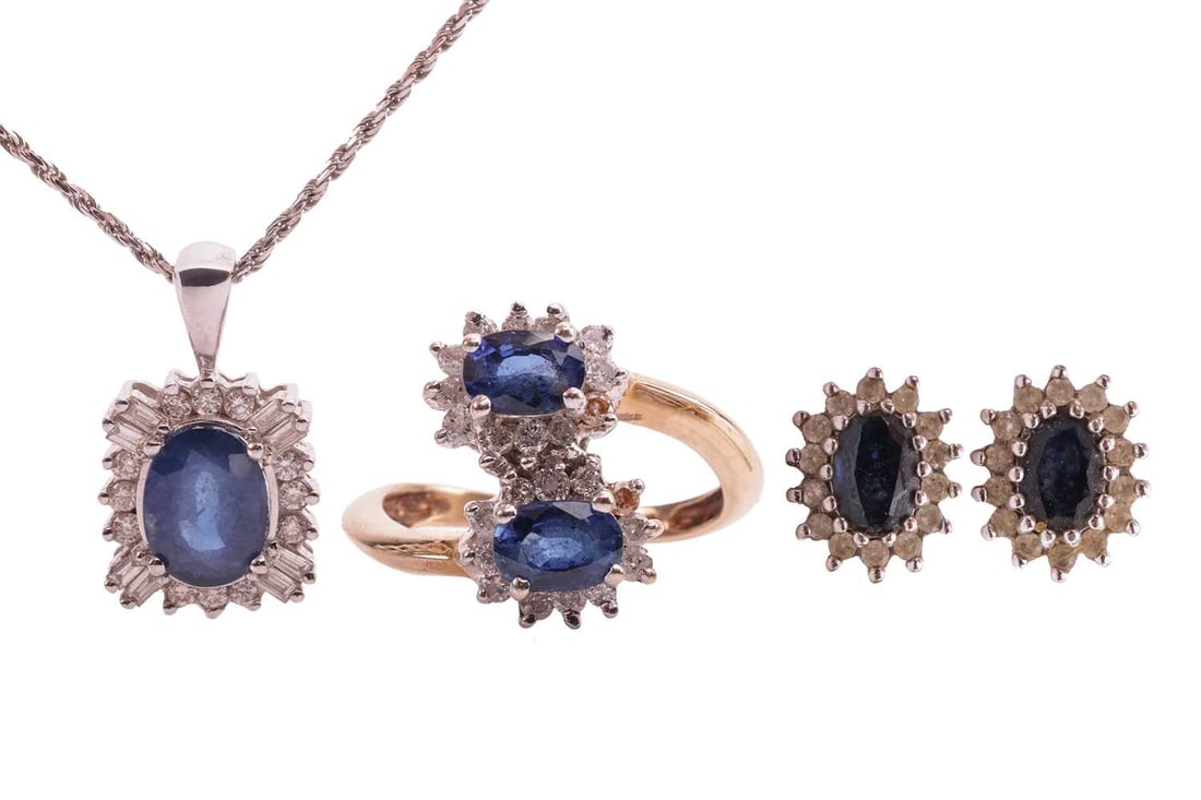A sapphire and diamond cluster ring, a pendant on chain and a pair of earrings; the cross-over ring: A sapphire and diamond cluster ring, a pendant on chain and a pair of earrings; the cross-over ring composed of two oval sapphire and diamond clusters, to a shank in yellow metal marked '9kt', ring he