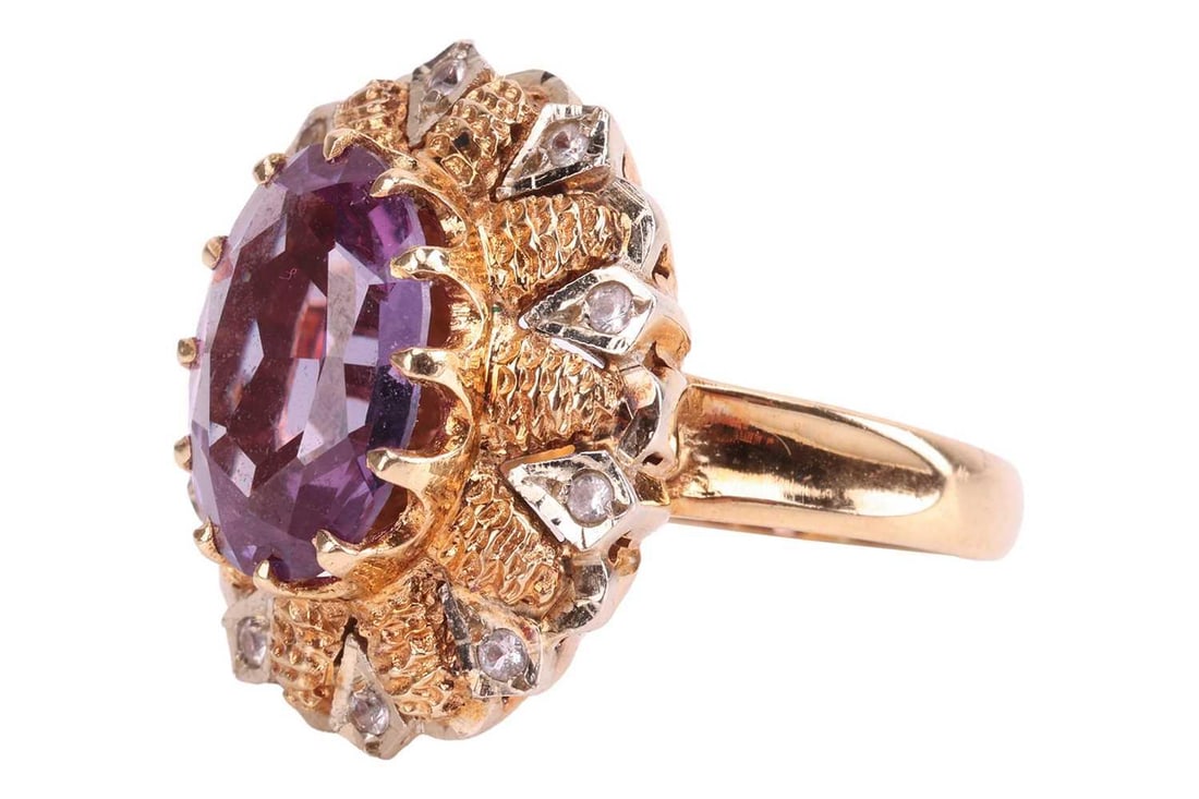 A synthetic colour change sapphire and white spinel dress ring, of bi metal cluster design, the: A synthetic colour change sapphire and white spinel dress ring, of bi metal cluster design, the central synthetic colour change sapphire approximately 13.9 x 9.9mm, claw set and flanked by a textured