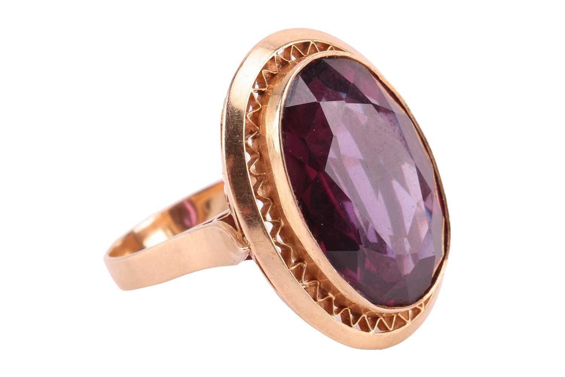 A synthetic colour-changing sapphire dress ring, comprising a large oval-cut synthetic: A synthetic colour-changing sapphire dress ring, comprising a large oval-cut synthetic colour-changing sapphire of 21.7 x 15.5 x 7.8 mm, collet-set to a corrugated surround, in a gallery pierced with
