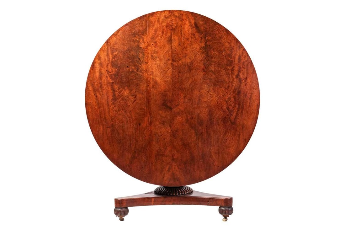 A George IV mahogany snap-top circular breakfast table, on a triform base with reeded bun feet. 129: A George IV mahogany snap-top circular breakfast table, on a triform base with reeded bun feet. 129 cm diameter x 78 cm height to the top, 70 cm knee height. Some undulation to the ground timber of th