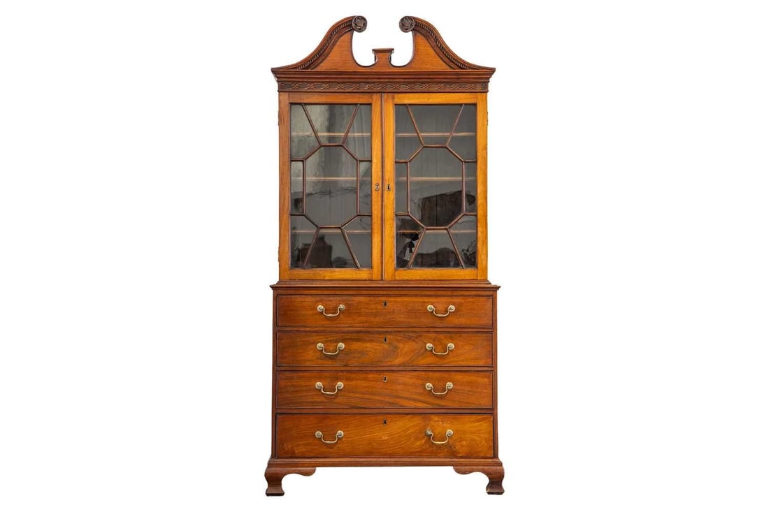 A George III padouk-wood secretaire-bookcase, the swan-neck pediment with dentil moulding and carved: A George III padouk-wood secretaire-bookcase, the swan-neck pediment with dentil moulding and carved foliate roundels, above two geometrically glazed doors enclosing shelves, the lower section with a 