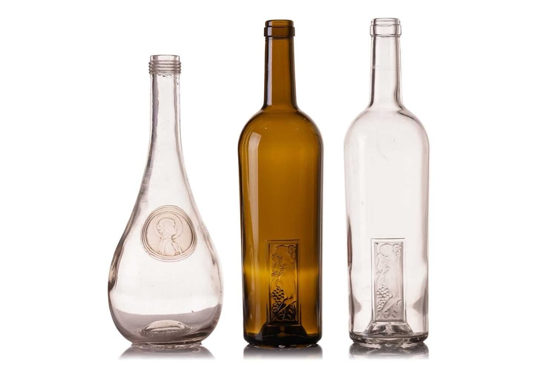 Two Lalique wine bottles, in clear and green glass, each marked 'Femme et Raisins Rene Lalique',: Two Lalique wine bottles, in clear and green glass, each marked 'Femme et Raisins Rene Lalique', with inset panel depicting a relief nude maiden, 30 cm high, together with a Lalique 'Clos Du Odile' te