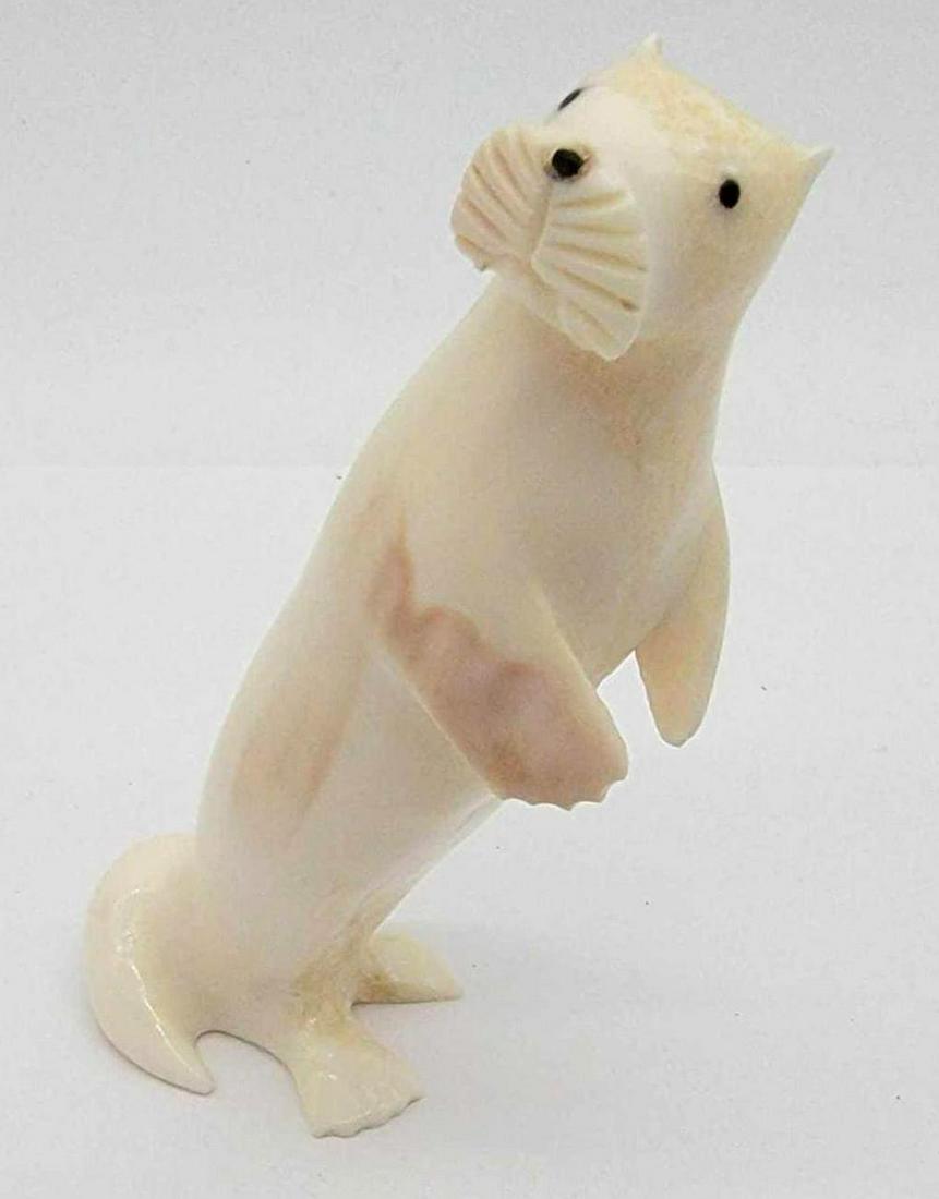 Walrus Tusk Sea Otter Carving by Mark Nupowlaktik: A standing sea otter figurine carved from Walrus tusk with baleen eyes and nose, signed "Mark N" on its underside and in good condition. Measures approximately 1.5" x 2" x 3.5" tal