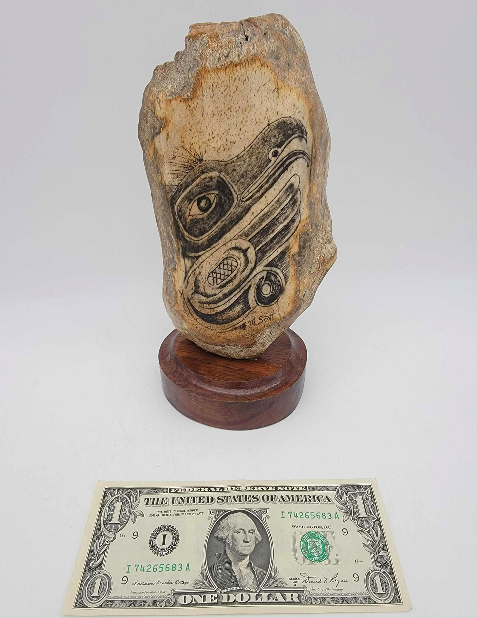 Walrus Bone w/Scrimshaw of NW Coast Style Raven by Mich: A section of Walrus skull adorned with detailed scrimshaw scene depicting a Northwest Coast style Raven signed for Michael Scott and mounted to a wood pedestal base. Measures approximately 8" tall