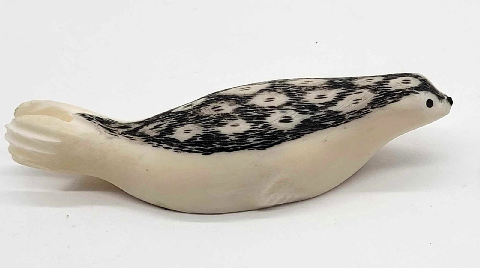 Scrimshaw Eskimo Ringed Seal Carving by Julian Iya: A Walrus tusk Seal carving with baleen eyes and nose plus scrimmed back detail, signed by Julian Iya. Measures approximately 3.25" x 1" x 0.75".