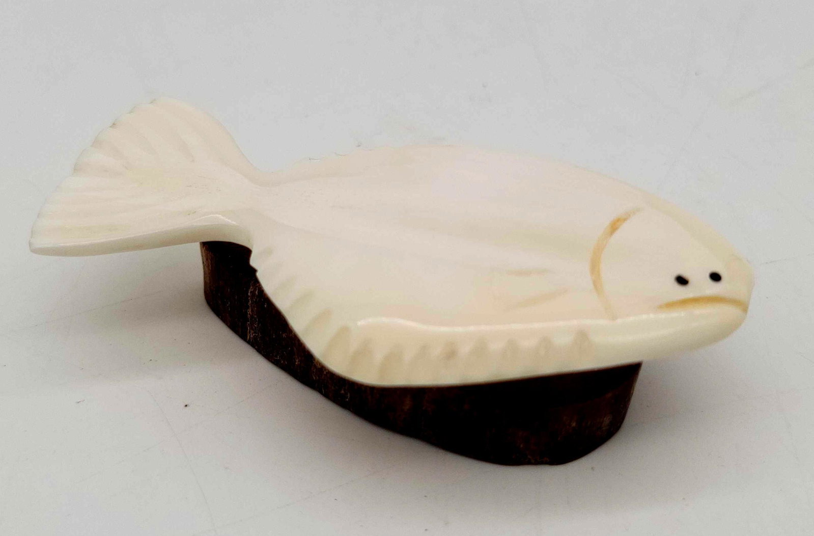Carved Walrus Tusk Halibut by Darin Slwooko: A Walrus tusk halibut carving mounted on a fossilized Walrus tusk base, detailed with baleen eyes and signed "D.S" on the bottom for Darin Slwooko. Remains in excellent condition; measures app