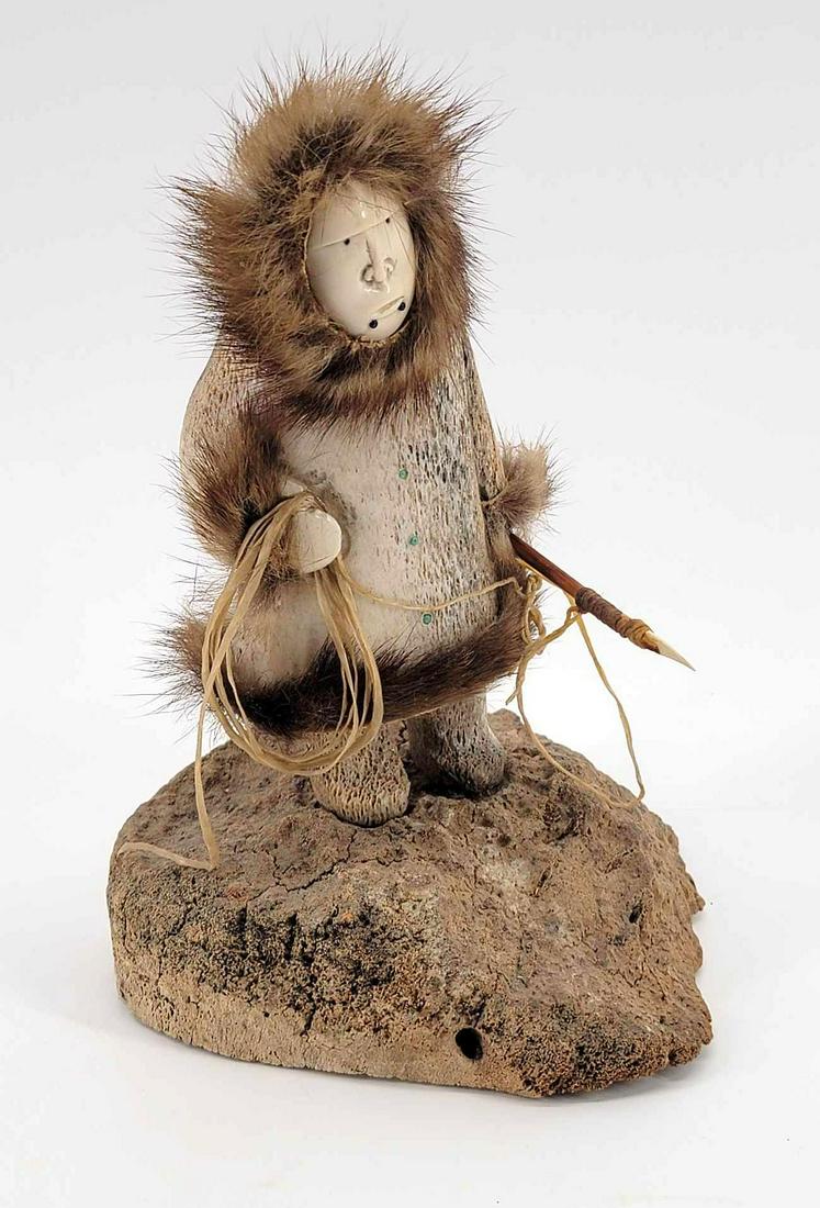 Carved Fossilized Bone & Tusk Activity Doll by Michael Scott: An activity doll depicting an Eskimo hunter with spear, fur trim, and gut rope, the body constructed from fossilized whalebone and the face mammoth tusk. Signed by the artist and 1997. Measures approx