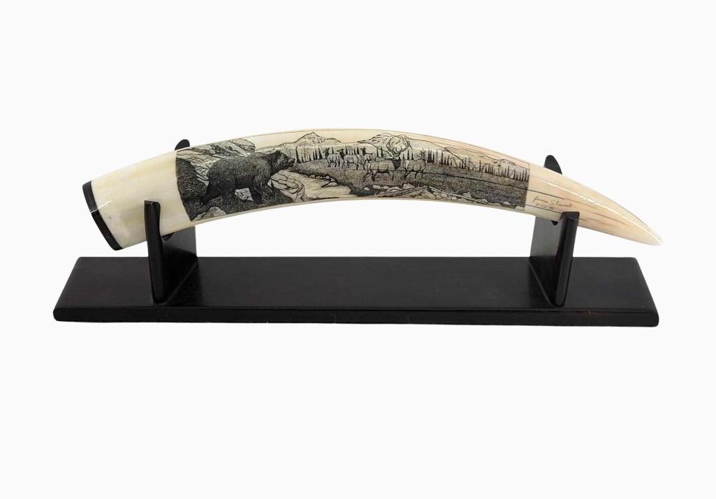 Highly Detailed Scrimshaw Walrus Tusk Depicting Elk & G: A mineralized walrus tusk featuring intricate scrimshaw depicting a grizzly bear looking onwards towards a group of five elk, the tusk capped with baleen and accompanied by a snuggly fitting wooden st