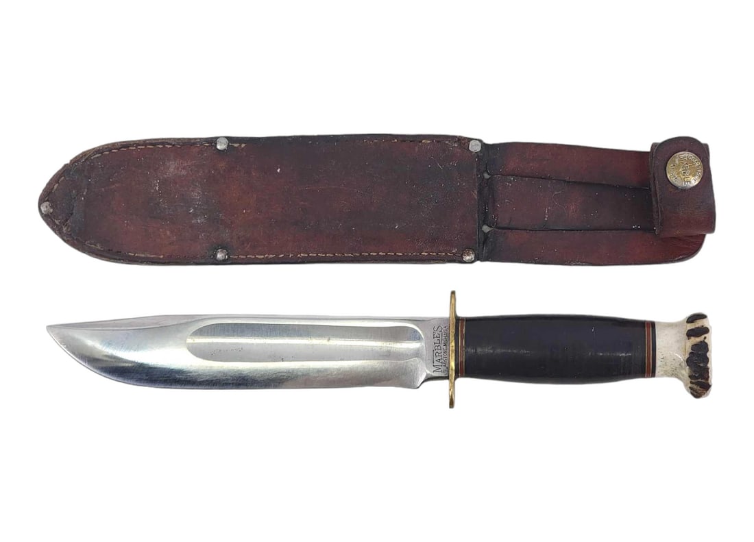 Marble's Ideal 6.5" Hunting Knife w/Sheath: A Marbles Ideal hunting knife with large blood groove, brass hilt, and stag pommel exposing a full-length rattail tang. Grip is of stacked leather and bound by spacers at either end. Housed in a leath