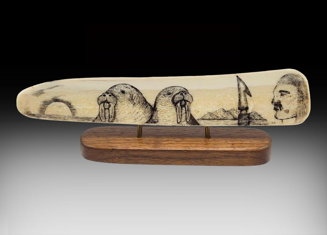 Scrimshaw Walrus Tusk w/ Cribbage Board & Oak Base: A walrus tusk fashioned with detailed scrimshaw scene of a pair of Pacific walrus, sun, mountains, water, and hunter with harpoon. The reverse side is drilled for use as a cribbage board. Tusk is moun