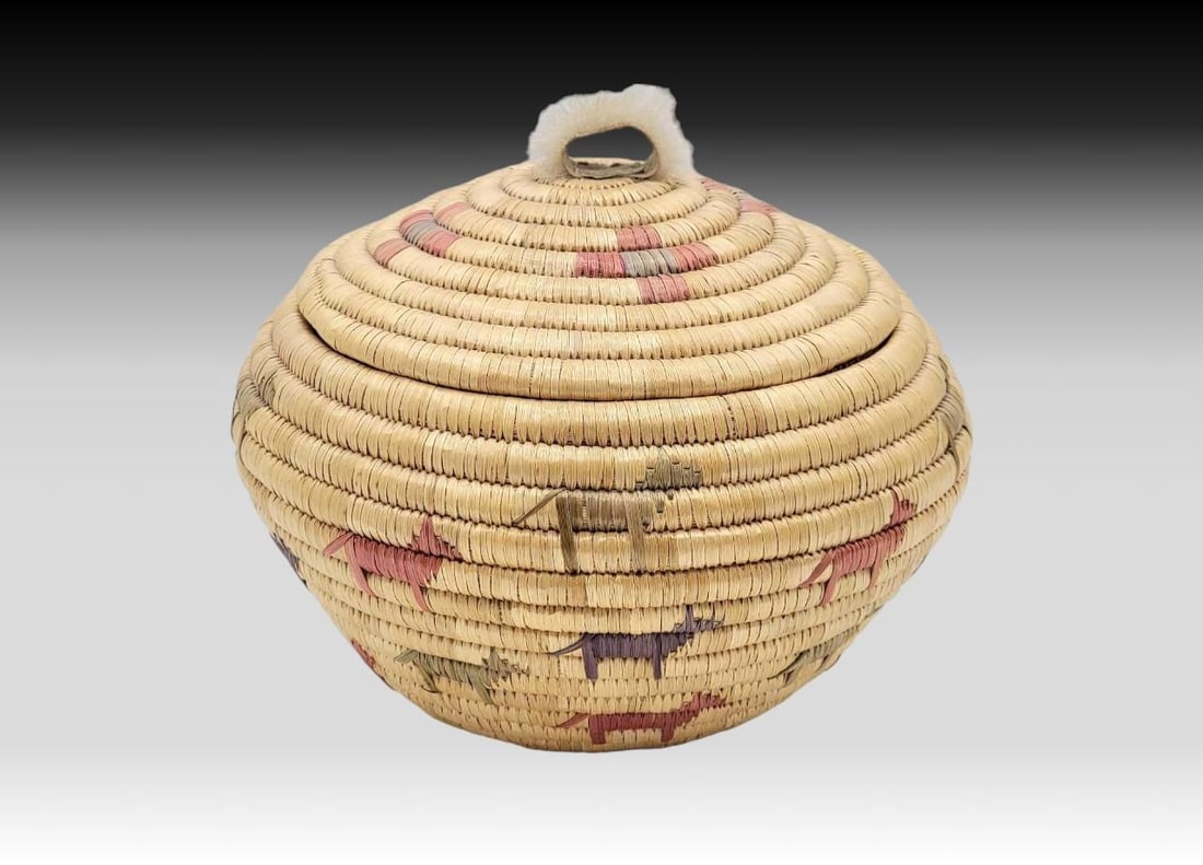 Pictorial Yup'ik Coiled Grass Basket w/Canine Design & Seal Fur Handle: A Yup'ik coiled grass lidded basket with embroidered polychrome canines in shades of red, green, and purple. The lid features coordinating polychrome geometric accents and is topped with a seal fu