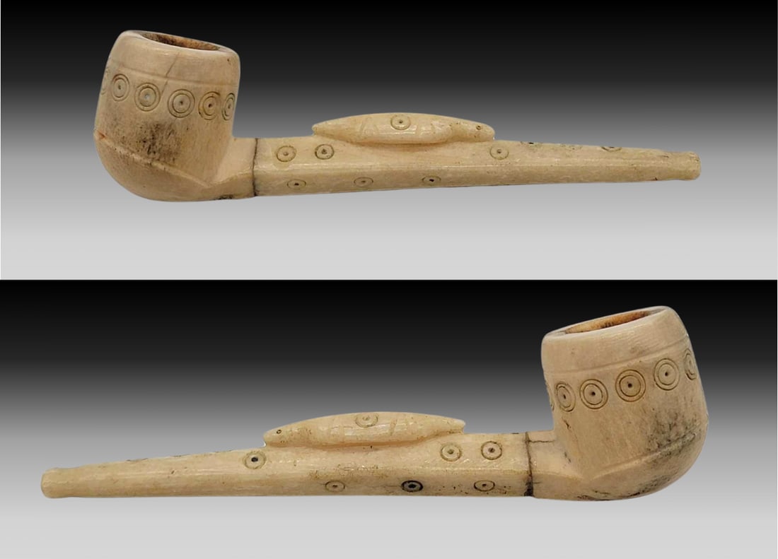 Antique Yup'ik Carved Walrus Tusk Smoking Pipe: An exceptional late 19th or early 20th century Yup'ik smoking pipe, the bowl carved from dense bone, the stem carved from walrus tusk. A ringed seal rests midway on top of the stem, and both the s