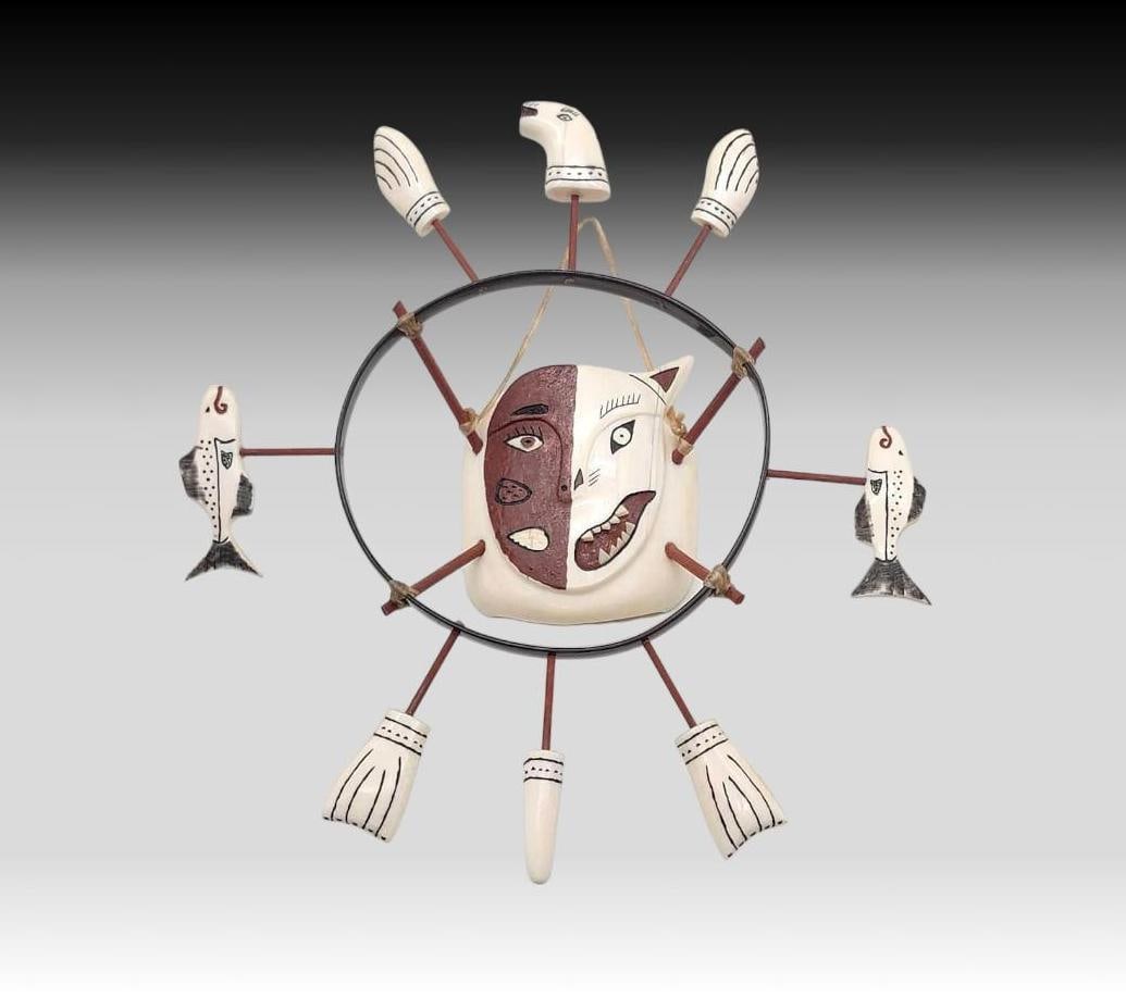 Yup'ik Walrus Tusk Spirit Mask - Lola Ferguson: A spirit wheel featuring a central painted transformational face carved from walrus tusk and suspended between four wooden rods upon a baleen circle. The wheel is further accented with eight carved an
