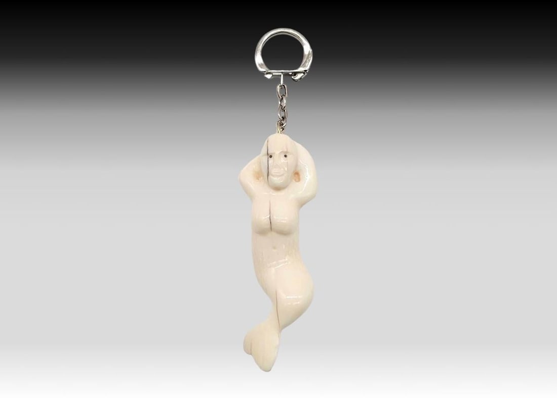 Walrus Tusk Mermaid Keychain: A carved and incised walrus tusk mermaid, attached to a small silvertone curb chain, terminating in a snap close keychain; back and front sides have longitudinal cracking as photographed. Measures app