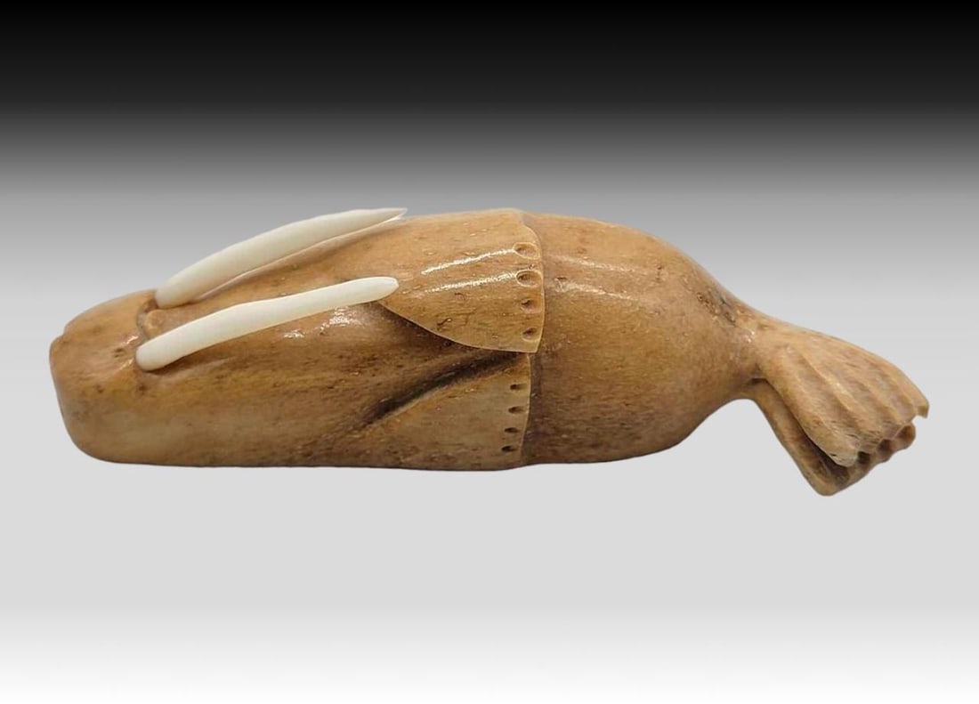 Walrus Jawbone Carved Walrus Figure: A fossilized walrus jawbone carved walrus with inset tusks, resting upon its side. Measures approximately 4" x 1" x 1" tall.