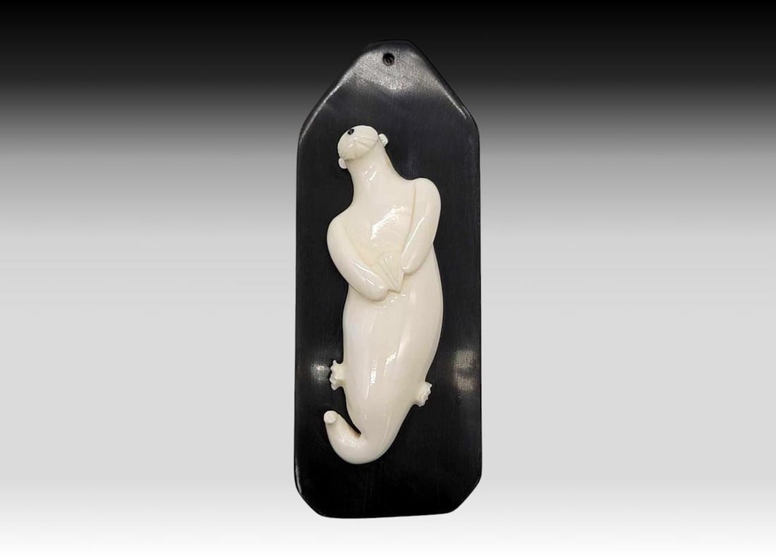 Walrus Tusk Sea Otter on Baleen Plaque - Uwetaq: A walrus tusk carved sea otter, resting upon its back and clutching a clam shell. Mounted upon a baleen plaque with hole for hanging and signed en verso by Yup'ik artist Uwetaq of Gambell, Alaska
