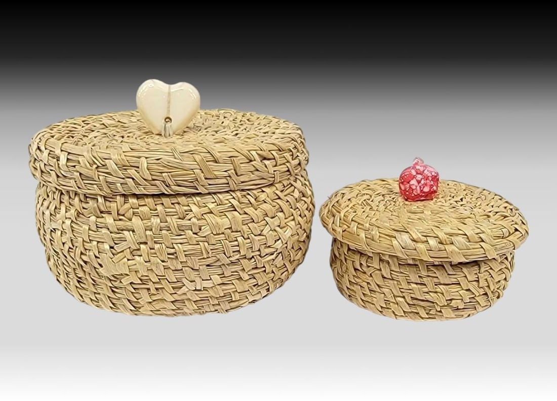 Yup'ik Coiled Grass Baskets w/ Finials - Stephanie Oittillian: Two Yup'ik coiled grass baskets, each with squat utilitarian shape and wide lids. The larger features a walrus tusk heart shaped finial, the smaller a pink finial. Attribution circa 2006 to Stepha