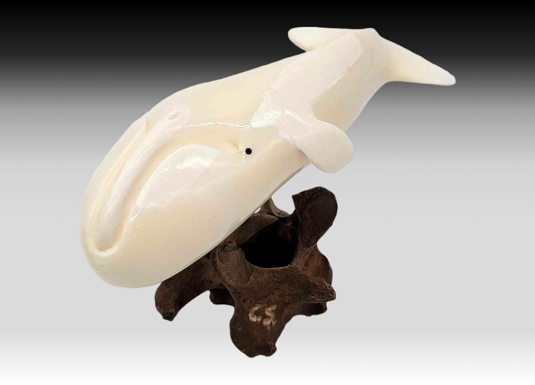 Walrus Tusk Whale Figurine on Vertebrae Base - Charles Slwooko: A carved walrus tusk figurine, depicting a whale, with inset baleen eyes; mounted via a baleen rod upon a small piece of vertebrae and initialed "C.S." on the underside for Yup'ik artist C