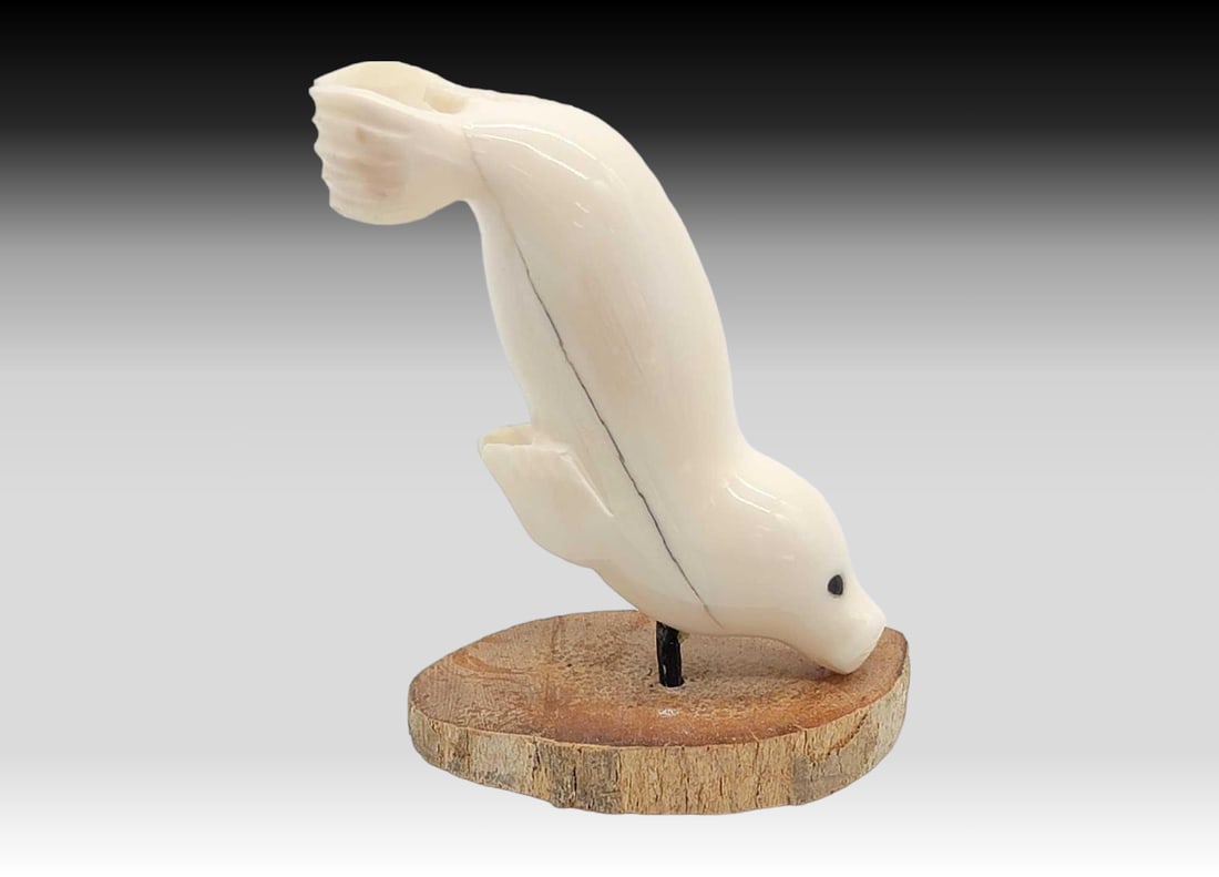 Walrus Tusk & Baleen Seal on Fossilized Tusk Base - Virgil Soonagrook: A walrus tusk carved in the shape of a seal, with inset baleen eyes, and mounted upon a slice of fossilized walrus tusk via a baleen rod. Signed on the underside for Yup'ik carver Virgil Soonagroo