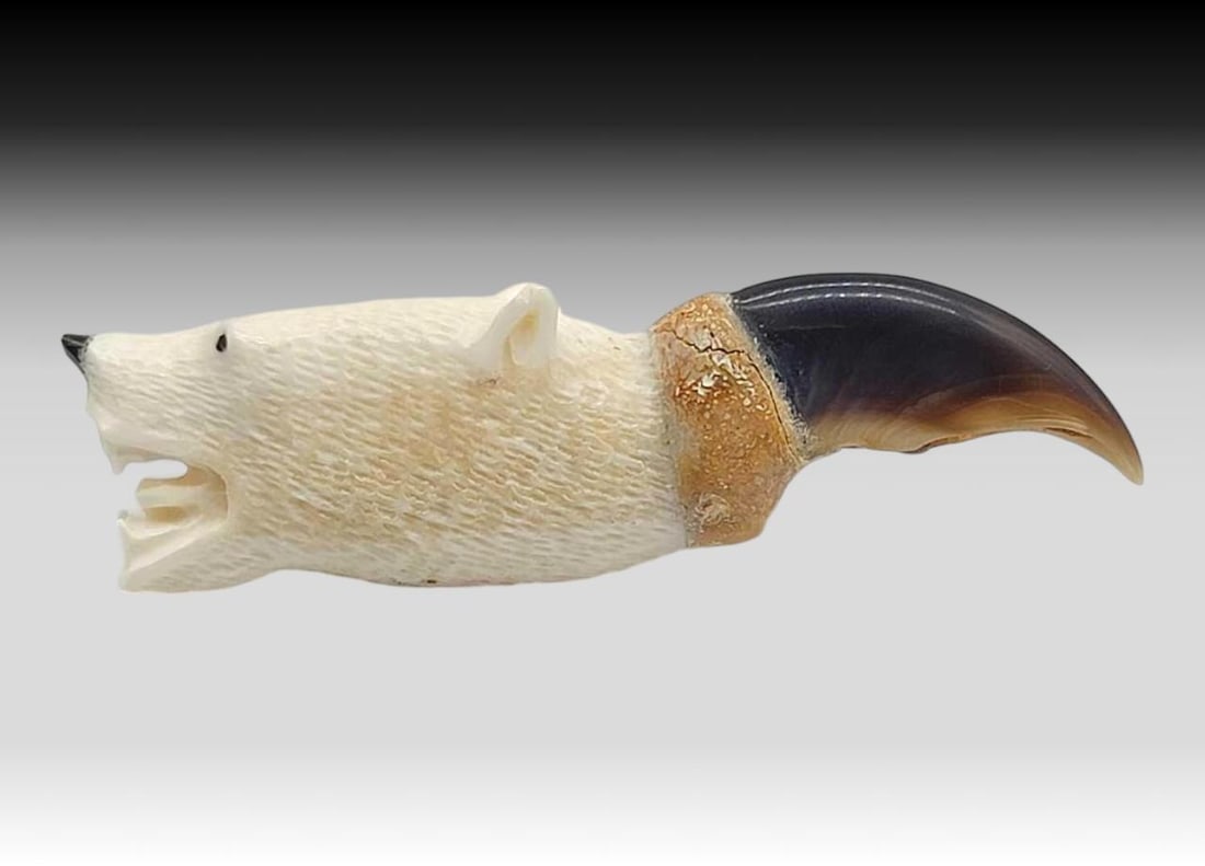 Polar Bear Claw w/ Scrimshaw Polar Bear Head: A polished polar bear clay in rich shades of cream, amber, and black, topped with a walrus tusk carved and incised polar bear head, accented with inset baleen eyes and nose. Claw has a fissure at the